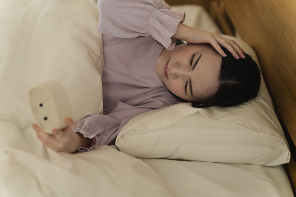 朝のベッドでスマートフォンを見る日本人女性